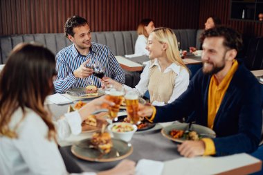 Çok ırklı arkadaşlar restoranda oturan, alkol içme, sohbet ve akşam yemeği için hamburger yeme.