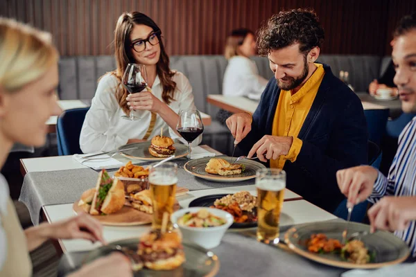 Amis multiethniques assis au restaurant, buvant de l'alcool, bavardant et ayant des hamburgers pour le dîner . — Photo