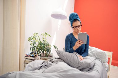 Yatak odasında yatakta otururken tablet kullanarak baş havlu ile Muhteşem esmer.