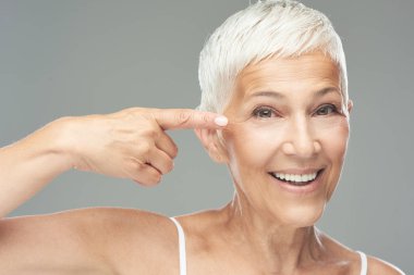 Güzel yaşlı kadının gözlerinin etrafındaki wtinkles'ı işaret eden headshot'ı. Güzellik fotoğrafçılığı.