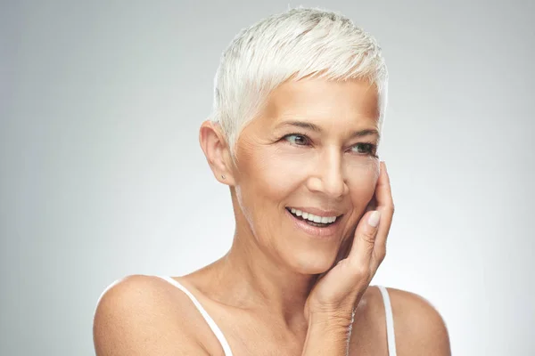 Bella donna anziana sorridente con i capelli corti grigi in posa di fronte a sfondo grigio. Foto di bellezza . — Foto Stock