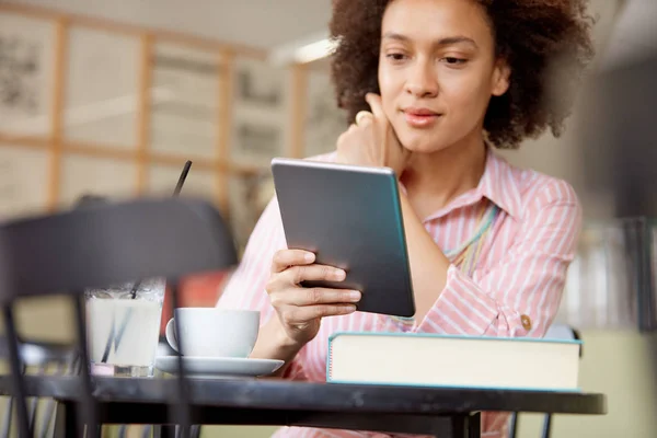 Attraktiv blandad ras kvinna i randig rosa klänning sitter i kafé och använder Tablet. — Stockfoto