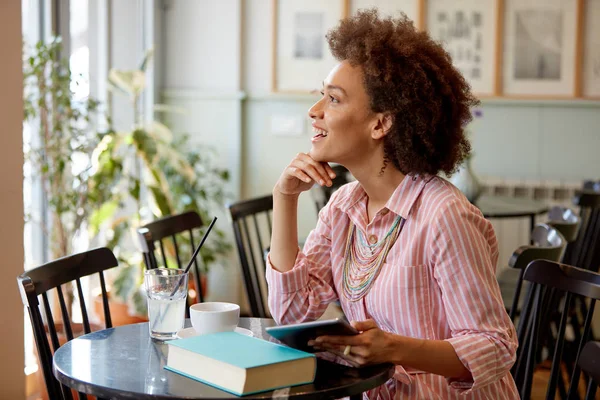 Aantrekkelijke mixed race vrouw in gestreepte roze jurk zitten in Cafe en het gebruik van Tablet. — Stockfoto