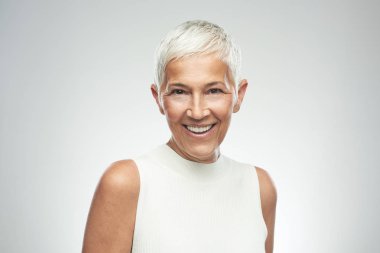 Gri arka plan önünde poz kısa gri saçlı güzel gülümseyen yaşlı kadın. Güzellik fotoğrafçılığı.