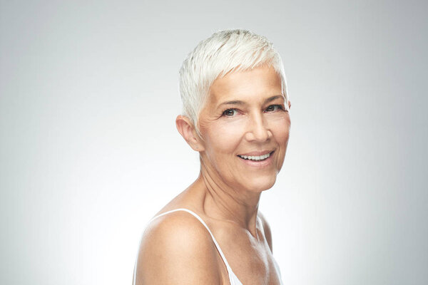 Улыбающаяся пожилая женщина с короткими седыми волосами позирует на заднем плане. Фотография красоты
.