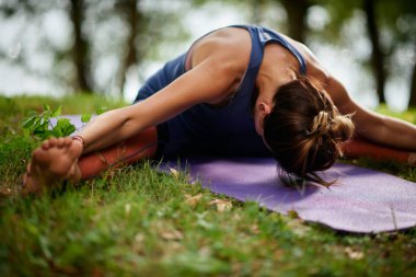 Adanmış Kafkas kadın su yakınında doğada paspas üzerinde oturan ve Seated Geniş Bacaklı İleri Bend yoga poz yapıyor.