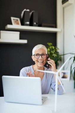 Muhteşem Kafkas yaşlı kadın ofiste otururken telefonda konuşuyor. Masada yel değirmeni modelleri ve dizüstü bilgisayar vardır. İş konseptini başlatın.