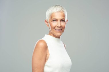 Gri arka plan önünde poz kısa gri saçlı güzel gülümseyen yaşlı kadın. Güzellik fotoğrafçılığı.
