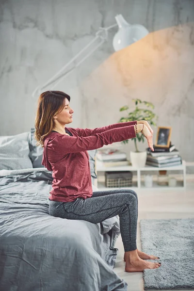 Encantadora morena caucásica sentada en la cama en el dormitorio y haciendo ejercicios de yoga . — Foto de Stock