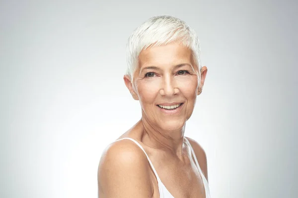 Hermosa mujer mayor sonriente con el pelo gris corto posando delante de fondo gris. Belleza fotografía . —  Fotos de Stock