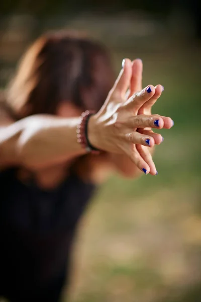 Mujer caucásica enfocada de pie en pose de yoga Guerrero III. Naturaleza exterior. Enfoque selectivo en las manos . — Foto de Stock