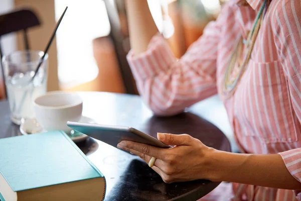 Attraente donna razza mista in abito rosa a righe seduto in caffè e utilizzando tablet . — Foto Stock