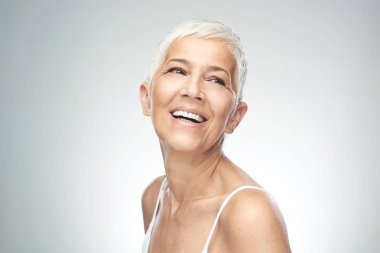 Gri arka plan önünde poz kısa gri saçlı güzel gülümseyen yaşlı kadın. Güzellik fotoğrafçılığı.