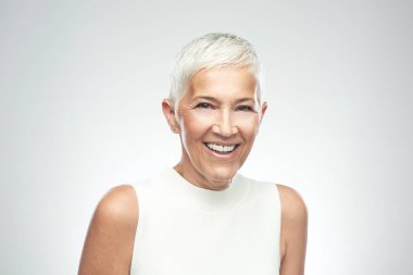 Gri arka plan önünde poz kısa gri saçlı güzel gülümseyen yaşlı kadın. Güzellik fotoğrafçılığı.