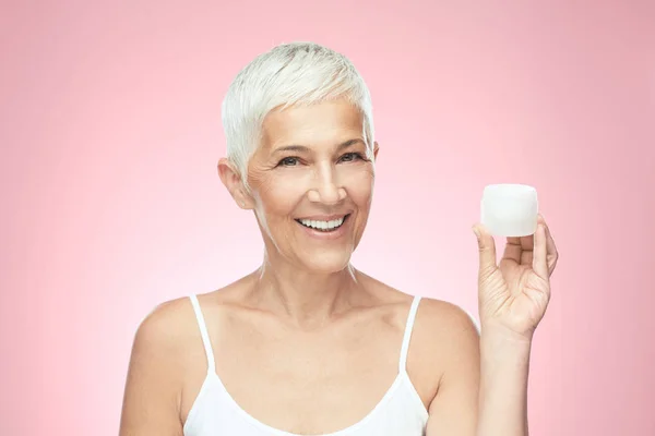 Eine zauberhaft lächelnde kaukasische Seniorin probiert eine neue Anti-Age-Creme aus und blickt in die Kamera. Schönheitsfotografie. — Stockfoto