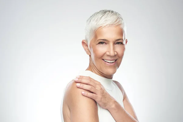 Hermosa mujer mayor sonriente con el pelo gris corto posando delante de fondo gris. Belleza fotografía . — Foto de Stock