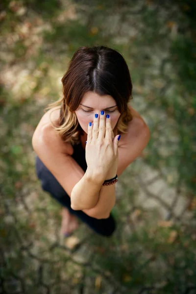 Vue du dessus de la femme caucasienne en tenue de sport debout sur le sol dans la nature dans la pose de yoga aigle. Focus sélectif sur les mains . — Photo