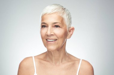 Gri arka plan önünde poz kısa gri saçlı güzel gülümseyen yaşlı kadın. Güzellik fotoğrafçılığı.