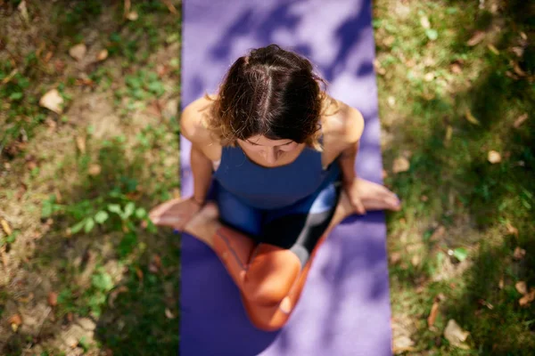 Вид з красивих Cucasian брюнетка, одягнені в спортивний одяг, сидячи на мат в природі в коліно купі йога позу. — стокове фото
