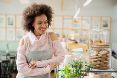 Pembe balıkçı yaka kazak ve çerez ile kavanoz yanında poz önlük ile çekici karışık ırk çalışanı. Pastane içi.