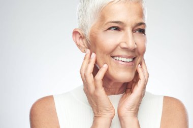 Gri arka plan önünde poz kısa gri saçlı güzel gülümseyen yaşlı kadın. Güzellik fotoğrafçılığı.