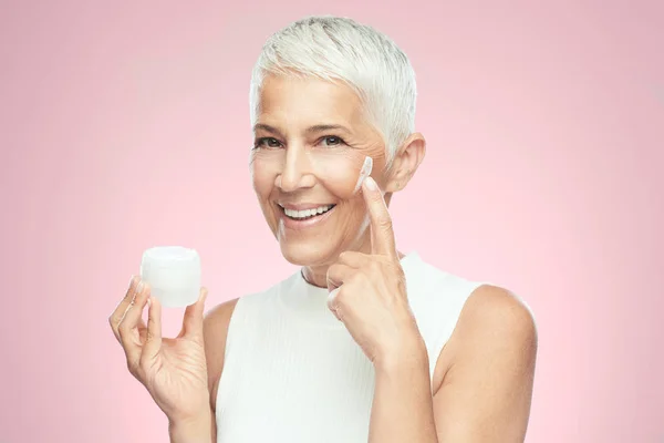 Prachtige glimlachend blanke Senior vrouw uitproberen van nieuwe anti-age crème. Beauty fotografie. — Stockfoto