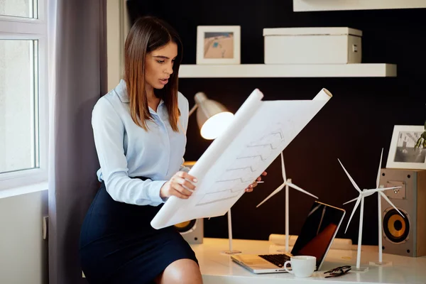 Привлекательная деловая женщина в рубашке и юбке сидит на столе в офисе и рассматривает планы. Концепция устойчивого развития . — стоковое фото