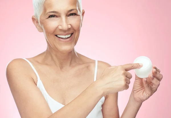 Prachtige glimlachend blanke Senior vrouw uitproberen van nieuwe anti-age crème en kijken naar de camera. Beauty fotografie. — Stockfoto