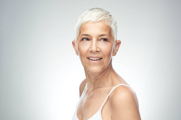 Улыбающаяся пожилая женщина с короткими седыми волосами позирует на заднем плане. Фотография красоты
.