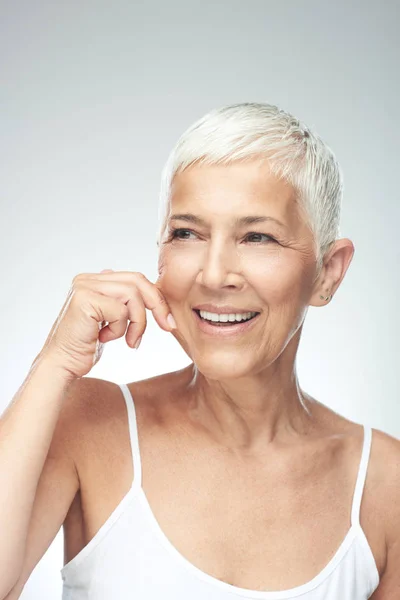 Prachtig glimlachend blanke Senior vrouw met korte grijze haren knijpen haar wang. Beauty fotografie. — Stockfoto