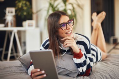 Yatak odasında yatakta mide yatan ve tablet kullanarak kazak Çarpıcı esmer. Sabah saati.