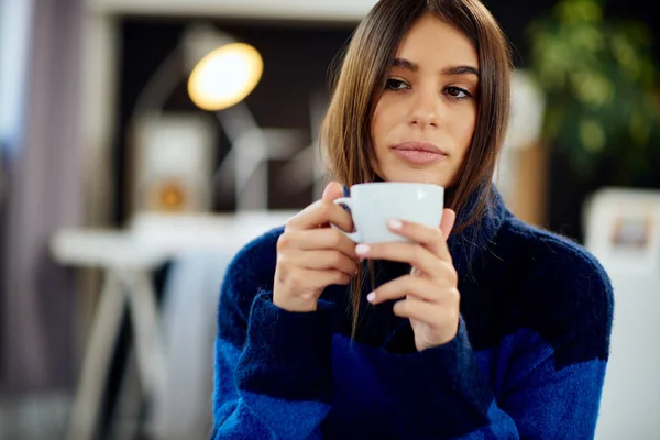 Charmante brunette in blauwe trui zittend in de slaapkamer in de ochtend en koffie drinken. — Stockfoto