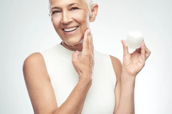 Prachtige glimlachend blanke Senior vrouw uitproberen van nieuwe anti-age crème. Beauty fotografie. — Stockfoto