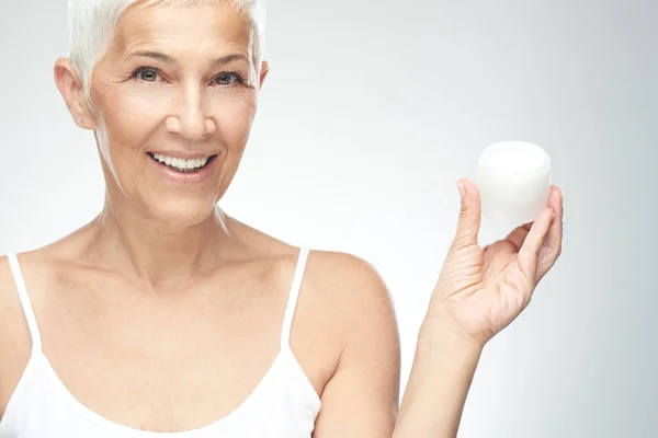 Gorgeous smiling Caucasian senior woman trying out new anti age cream. Beauty photography. — Stock Photo, Image