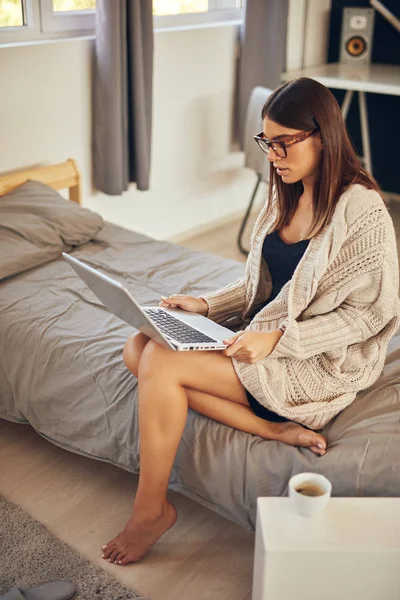 Attraktiva kaukasiska brunett sitter på sängen i sovrummet och använda laptop. — Stockfoto