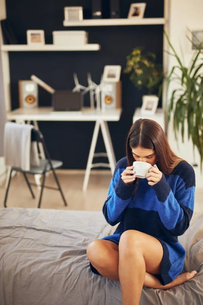 Charmante brunette in blauwe trui zittend in de slaapkamer in de ochtend en koffie drinken. — Stockfoto
