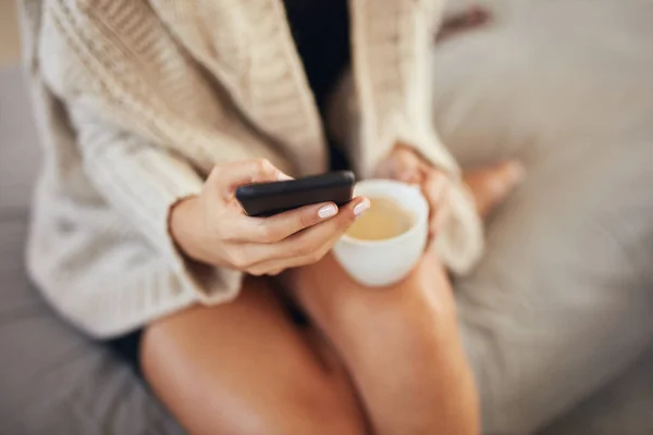 Widok z góry kaukaska kobieta za pomocą smartfona i trzymając filiżankę kawy podczas siedzenia na łóżku rano. — Zdjęcie stockowe