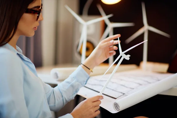 Businesswoman in suit sitting in office and holding windmill model. On desk are coffee, documentation and laptop. Sustainable concept. — Stock Photo, Image