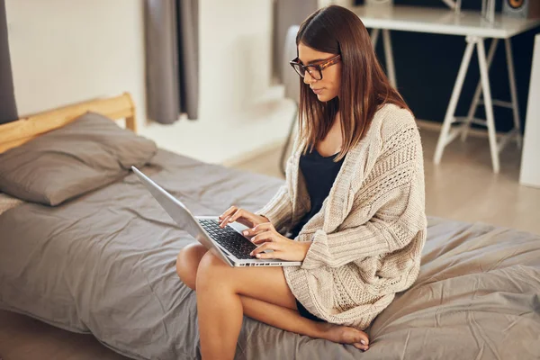 Atrakcyjna kaukaski brunetka siedzi na łóżku w sypialni i za pomocą laptopa. — Zdjęcie stockowe