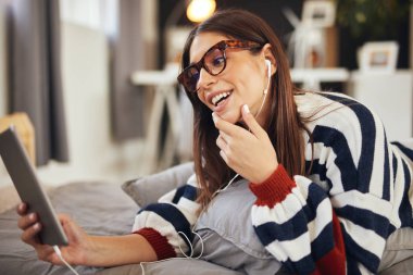 Yatak odasında yatakta mide yatan ve tablet kullanarak kazak Çarpıcı esmer. Sabah saati.