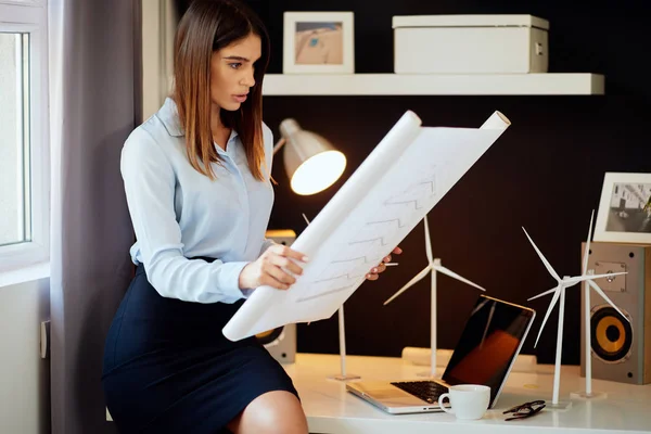 Aantrekkelijke zakenvrouw in overhemd en rok zittend op het Bureau in kantoor en kijken naar plannen. Concept duurzame ontwikkeling. — Stockfoto