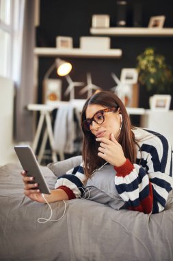 Yatak odasında yatakta mide yatan ve tablet kullanarak kazak Çarpıcı esmer. Sabah saati.