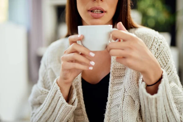 Blanke vrouw gekleed in beige trui zittend op bed en het houden van verse koffie in de ochtend. — Stockfoto