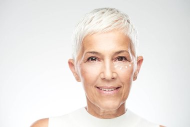 Muhteşem gülümseyen Kafkas yaşlı kadın yeni anti age krem çalışıyor ve kamera bakıyor. Güzellik fotoğrafçılığı.