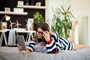 Yatak odasında yatakta mide yatan ve tablet kullanarak kazak Çarpıcı esmer. Sabah saati.