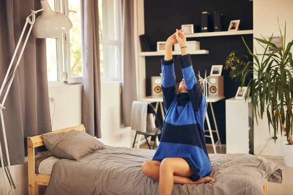 Hermosa morena caucásica en suéter azul sentada en la cama en el dormitorio y estiramiento. Hora de la mañana . — Foto de Stock