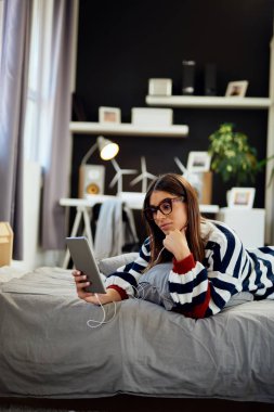 Yatak odasında yatakta mide yatan ve tablet kullanarak kazak Çarpıcı esmer. Sabah saati.