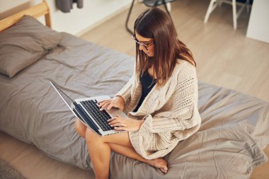 Çekici beyaz esmer yatak odasında yatakta oturan ve dizüstü bilgisayar kullanarak.