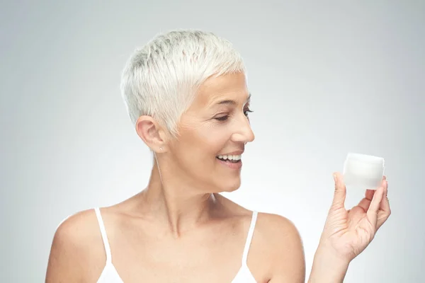 Prachtige glimlachend blanke Senior vrouw uitproberen van nieuwe anti-age crème. Beauty fotografie. — Stockfoto