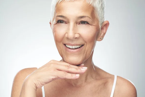 Hermosa mujer mayor sonriente con el pelo gris corto posando delante de fondo gris. Belleza fotografía . —  Fotos de Stock